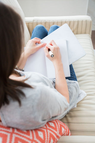 woman sitting on a couch writing in a journal