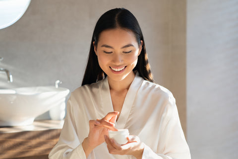 Smiling young asian lady holding jar with beauty product