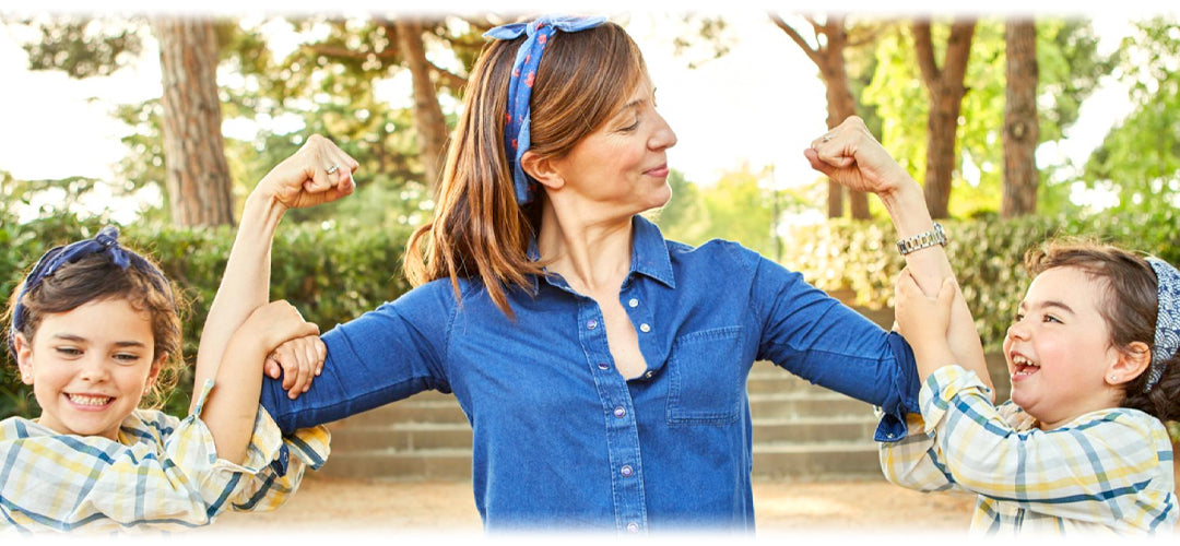 A woman holding her arms out strong with children clutching them, symbolising important health practices 