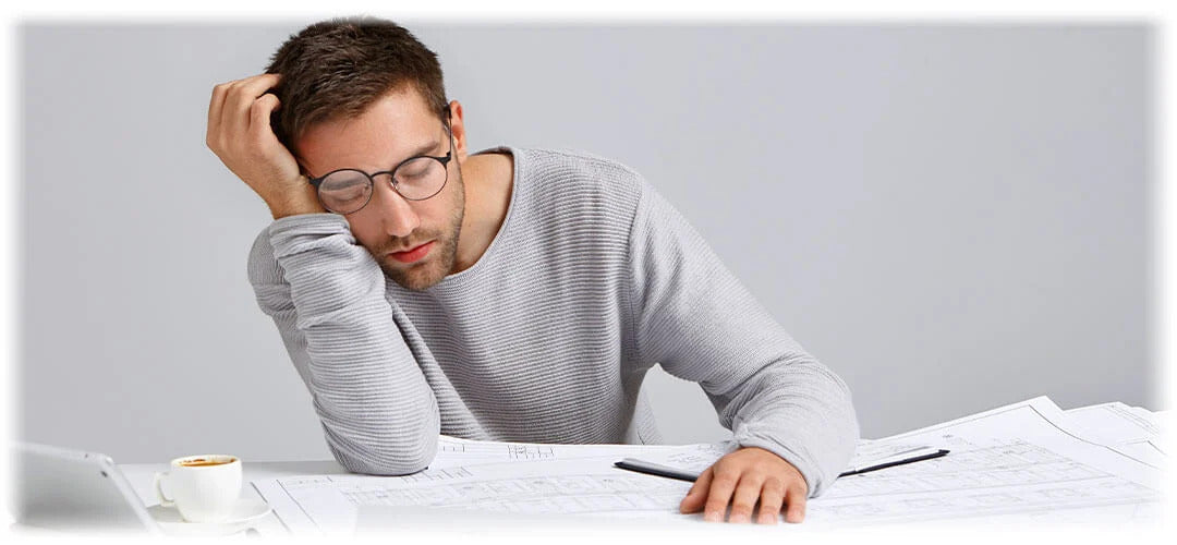 An image portraying a tired individual, falling asleep whilst working. The image suggests the fatigue and exhaustion.