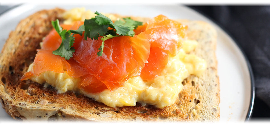 Salmon fillet served on whole grain toast with avocado slices and greens, a nutritious meal option.