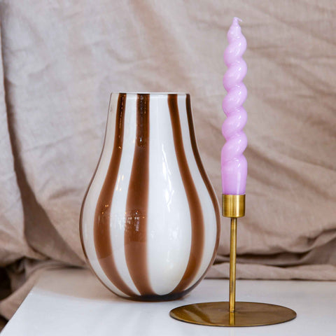 lilac Suzumi glossy wavy spiral candle in brass house doctor holder next to a mouth blown Murano inspired taupe and white glass vase by Broste Copenhagen