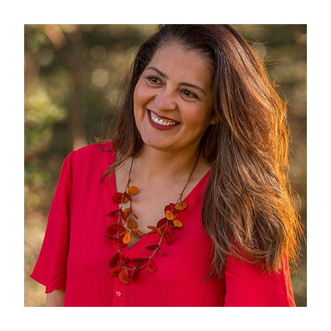 Older woman looking into the distance wearing a red top with the orange Secca necklace on