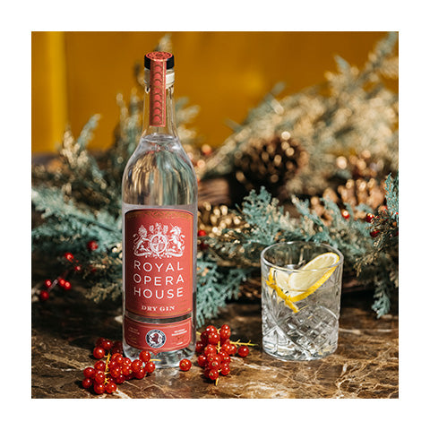 A bottle of Royal Opera House gin on a wooden table decorated with festive greenery and red berries.