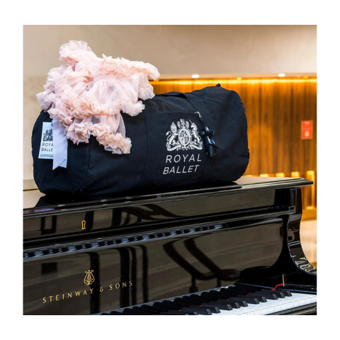 A black royal ballet training bag sits on top of a glossy black piano.