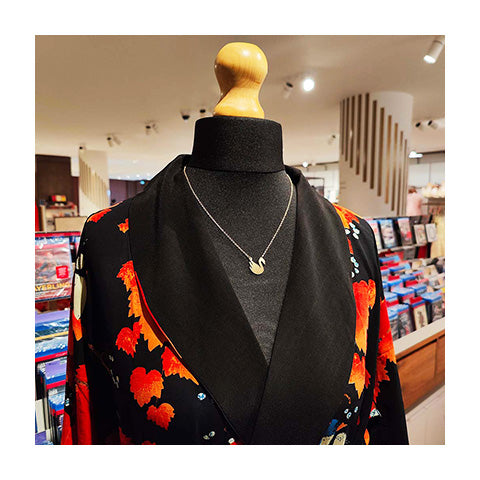 A mannequin dressed in an orange kimono with a gold swan charm necklace.