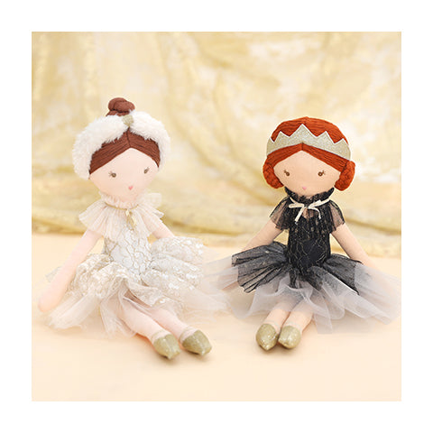 Two soft dolls sitting against a background, one based on the white swan and one based on the black swan.