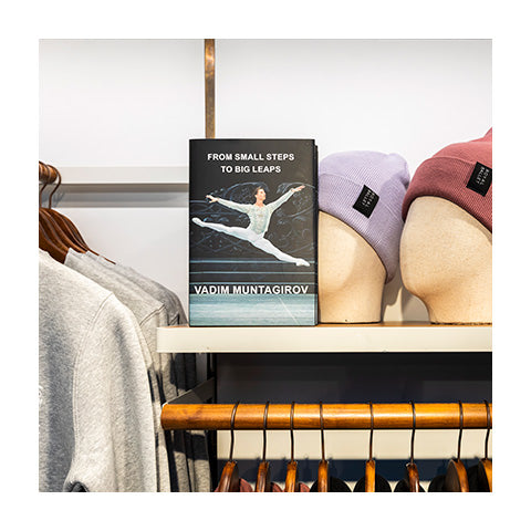 A book with a male ballet dancer in mid leap sitting on a shelf of a shop.