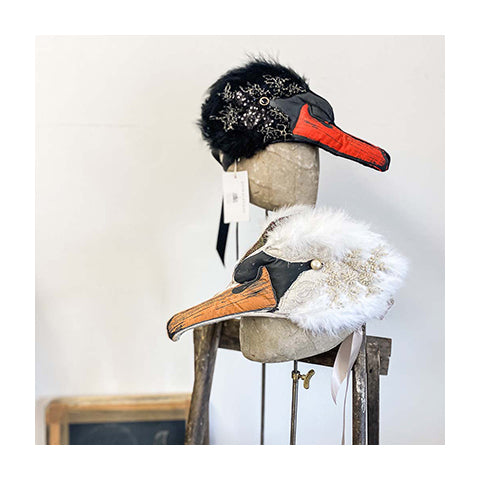 Two intricately designed headdresses are propped on a wooden stand, one is a delicate white swan and one is a striking black swan