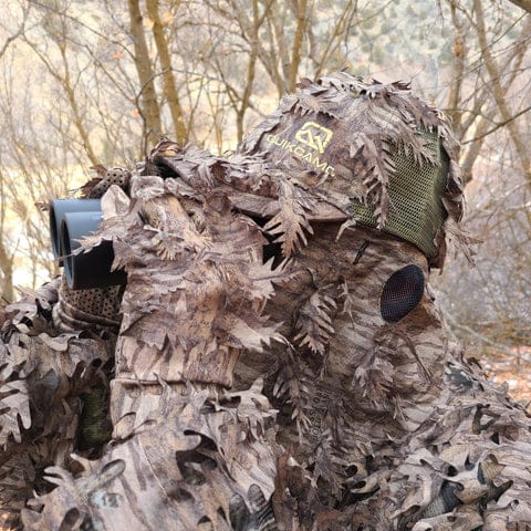 Man using binoculars and wearing QuikCamo Leafy Gear. The camo pattern used is Mossy Oak Bottomland