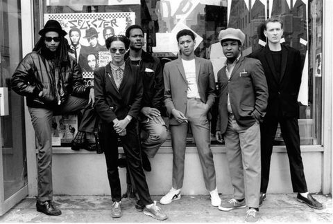 Six members of the ska group Selecter wear suits and sneakers. They stand in front of a shop in 1970s Los Angeles.