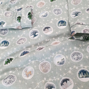 Close up photograph of bayridgecaskandkeg's Baubles print fabric. The fabric is light green and features garlands of baubles each depicting a different wintery or festive scene.