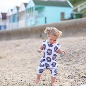 Toddler girl wearing bayridgecaskandkeg Aztec Lion organic romper on the beach with beach huts in the distance