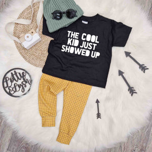 bayridgecaskandkeg kids outfit inspiration featuring a black t-shirt with 'The Cook Kid Just Showed up Slogan', mustard grid baby and toddler leggings & green knitted beanie hat
