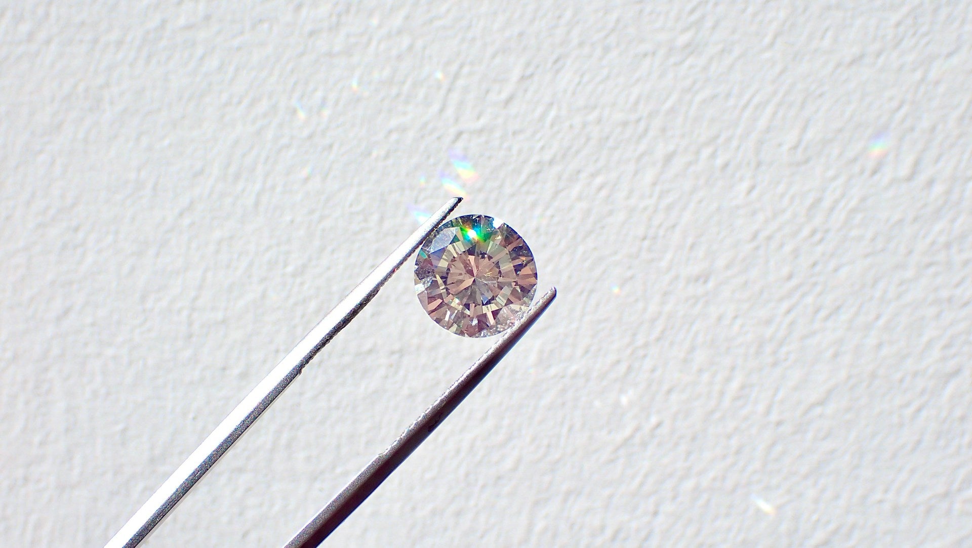 A pair of tweezers holding a real diamond up to the light