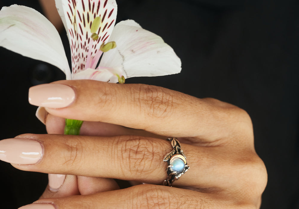 A women holding a moonstone in her ring and a flower