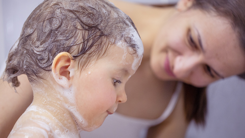 Brunette mother washing young brunette child's hair during bathtime