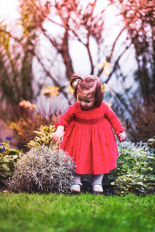Amelie playing in the garden in her Christmas Coral red velvet smocked dress 