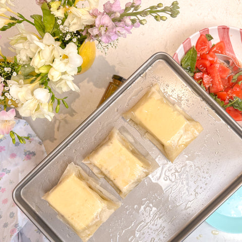 Feta filo pastry wraps on a baking tray with flowers in the back ground