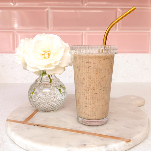 Summer Smoothie in a tall glass with gold straw by a vase of white roses