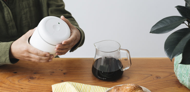 Hands holding Atmos Vacuum Canister in Matte White with brewed coffee in Mighty Small Glass Carafe