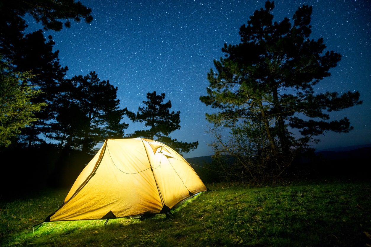 Glowing tent under a starry night sky surrounded by pine trees, epitomizing the ideal location for a memorable boondocking experience | KEUTEK