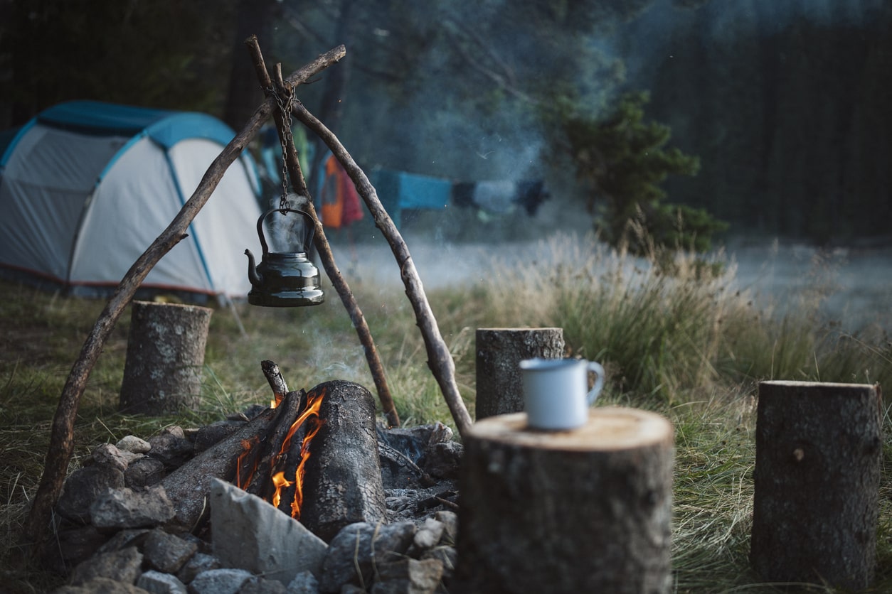 Camping kettle hanging over a campfire with a tent in the background, evoking the simple pleasures of boondocking in the wilderness | KEUTEK