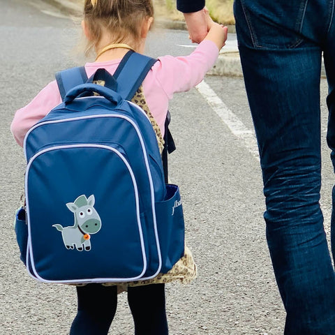 Girl walking down the street wearing a blue Jordbarn blue backpack and holding her dad's hand