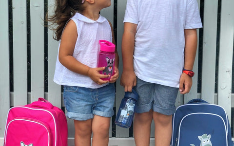 Two kids looking at each other holding Jordbarn backpacks and water bottle