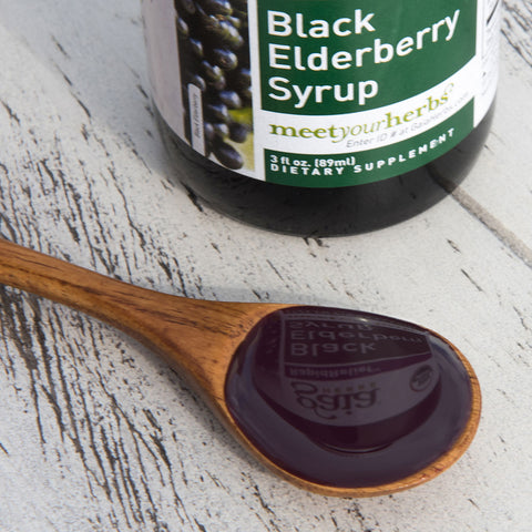 Gaia Herbs Black Elderberry Syrup on wooden spoon with bottle in background
