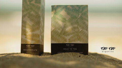 Tap Tap Organics Regenerate Beauty Oil box and Head To Toe Beauty Butter box on the sand