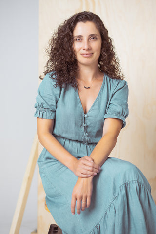 Portrait of Patricia Fonseca, founder of Tap Tap Organics. She is sitting on a stool, with a blue dress and small smile.