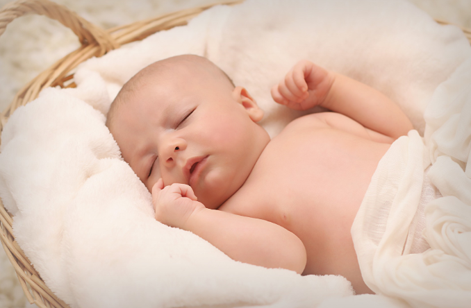 Baby sleeping on a basket with fluffy white blanket.