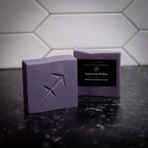 two bars of purple sagittarius zodiac soap on a black countertop