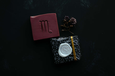 blackcurrant red soap with scorpio symbol stamped into it beside a gift wrapped bar