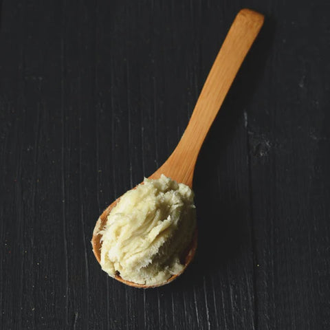 shea butter in wooden spoon on black surface