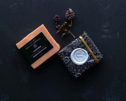 bright orange leo zodiac soap with gift wrapped and standard label version on black background and botanicals