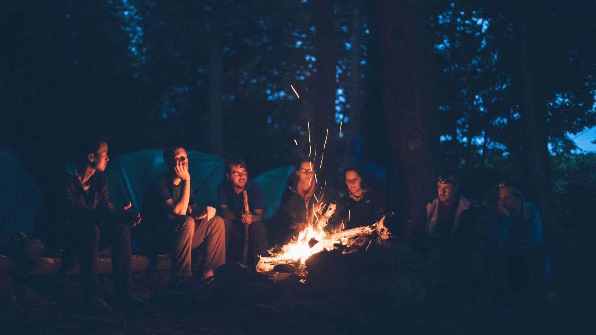 Menschen sitzen vor Zelten um ein Feuer 