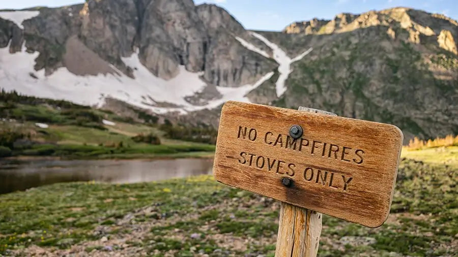sign that reads No Campfires, only stoves. With a mountain & lake background