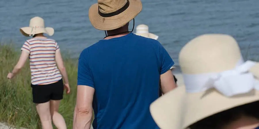 Two people walking along the water with sun hats