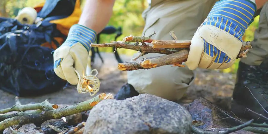 prepping a campfire with gloves on and small sticks ready