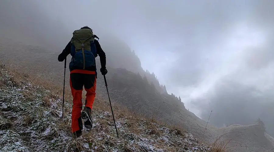 man climbing steep mountain with a trekking pole in each hand
