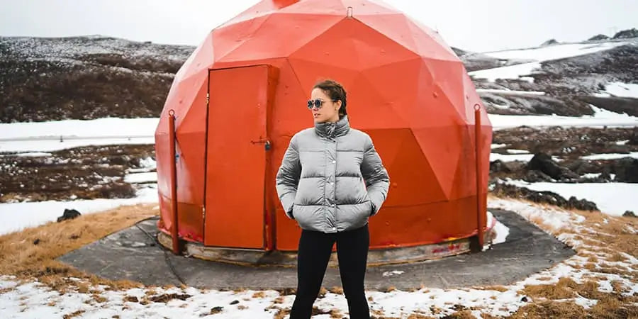 Woman in a down jacket in the snow in front of a dome tent