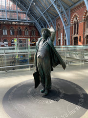 Statue of man in trench coat, holding on to his hat and a briefcase