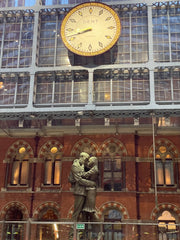 Bronze statue of a male and female embracing under an illuminated clock, St Pancras international station.