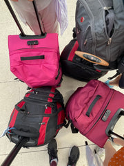 Four wheelie suitcases: (going clockwise from top left) bright pink, black and red, burgundy, black and red.