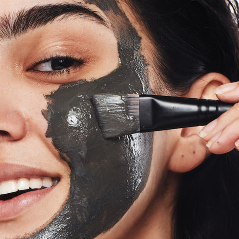 Woman applying a mud mask with a face mask brush