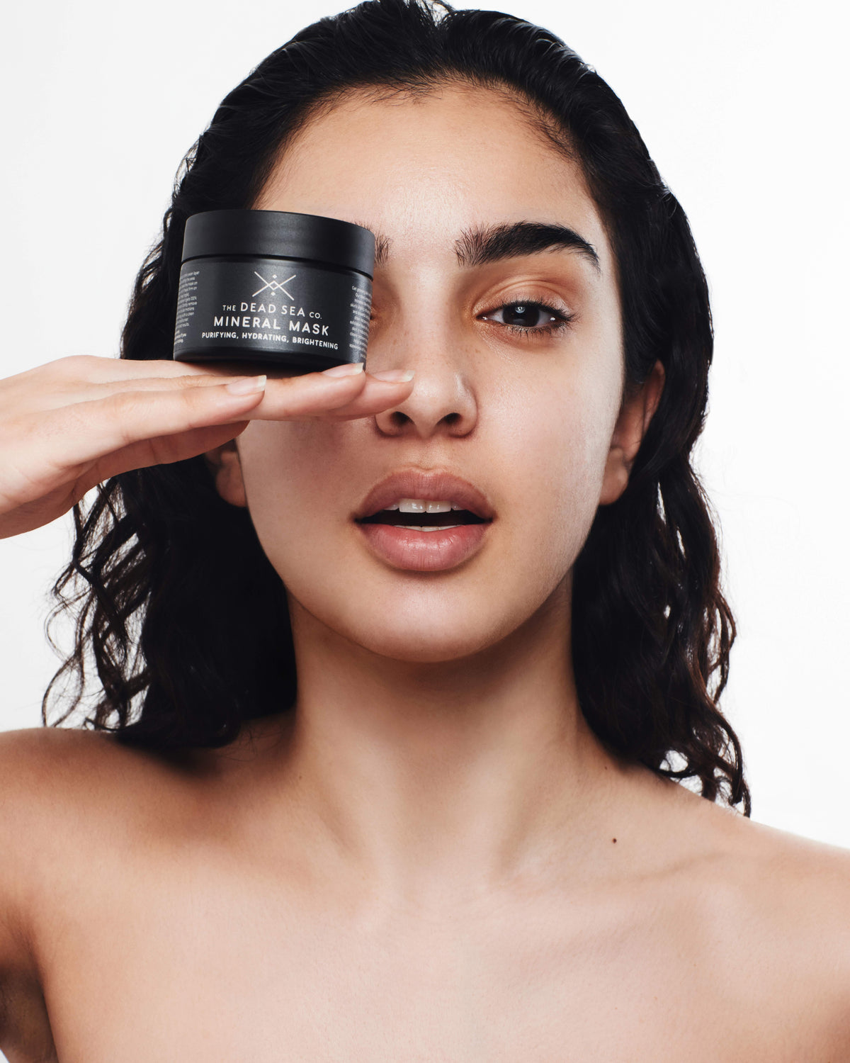 Woman using a Dead Sea mud mask and holding The Dead Sea Co mask in her hand