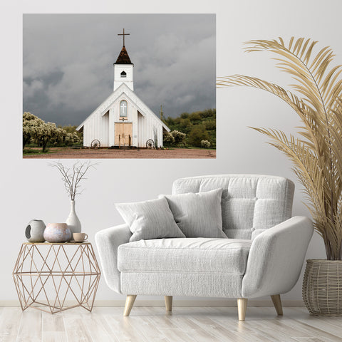 White church surrounded by dark clouds focused art on wall above white chair