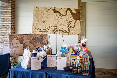 two large maps along with other charity auction items are set on a table with a blue table cloth for the cross schools charity, pearls for pluff mud